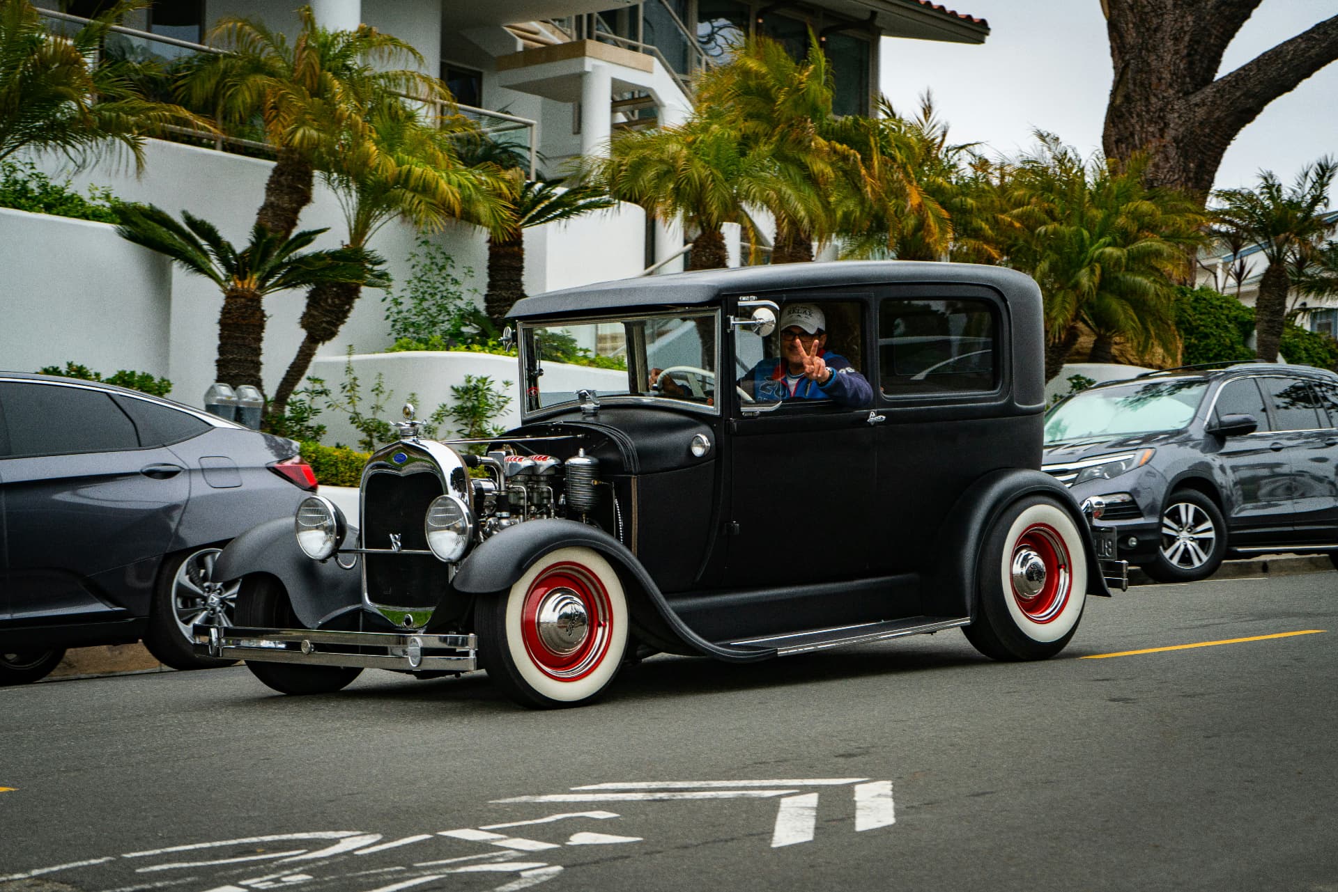 A vintage hot rod rolling down a palm-lined Laguna Beach street