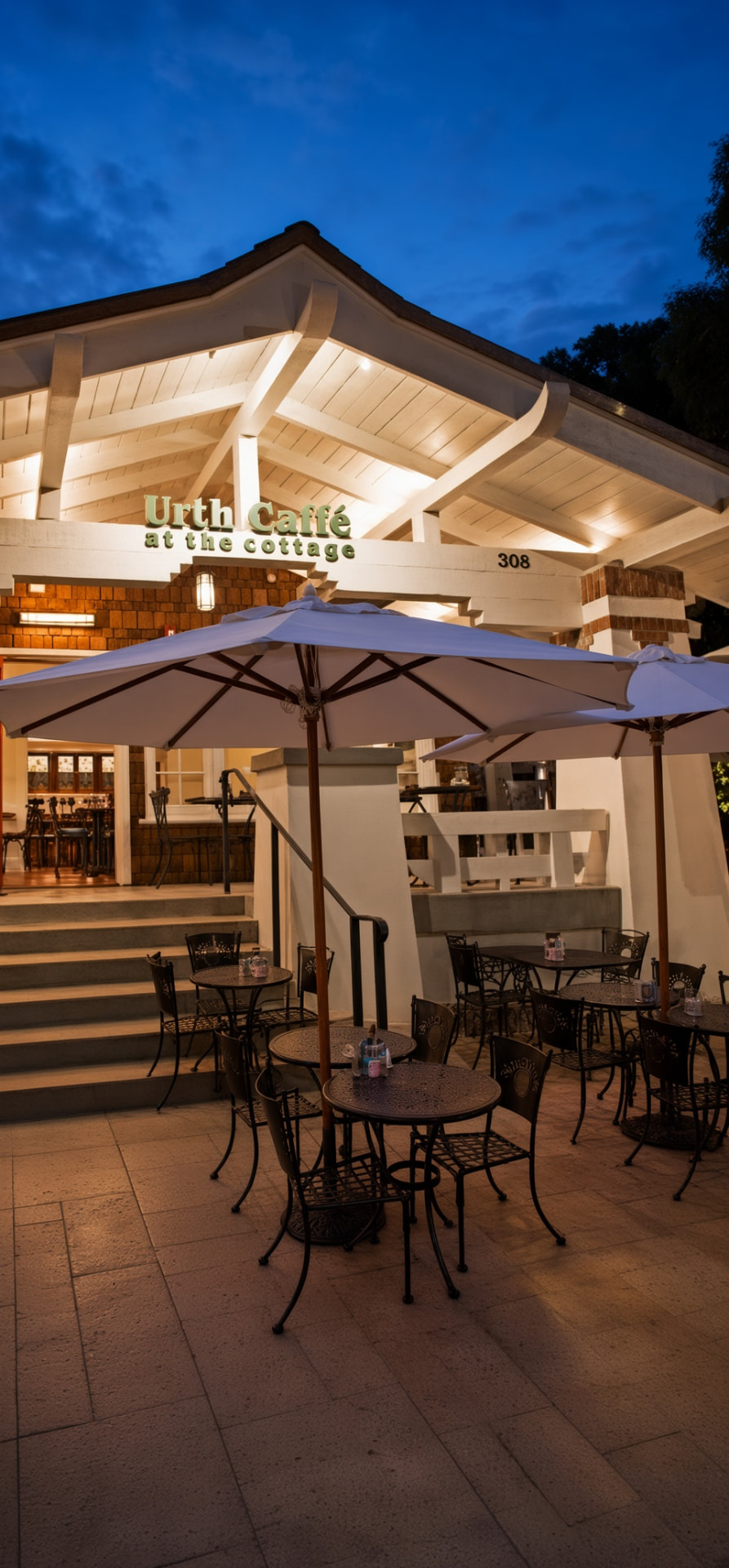Urth Caffé at the Cottage on Coast Highway at dusk with lit patio umbrellas and cafe tables