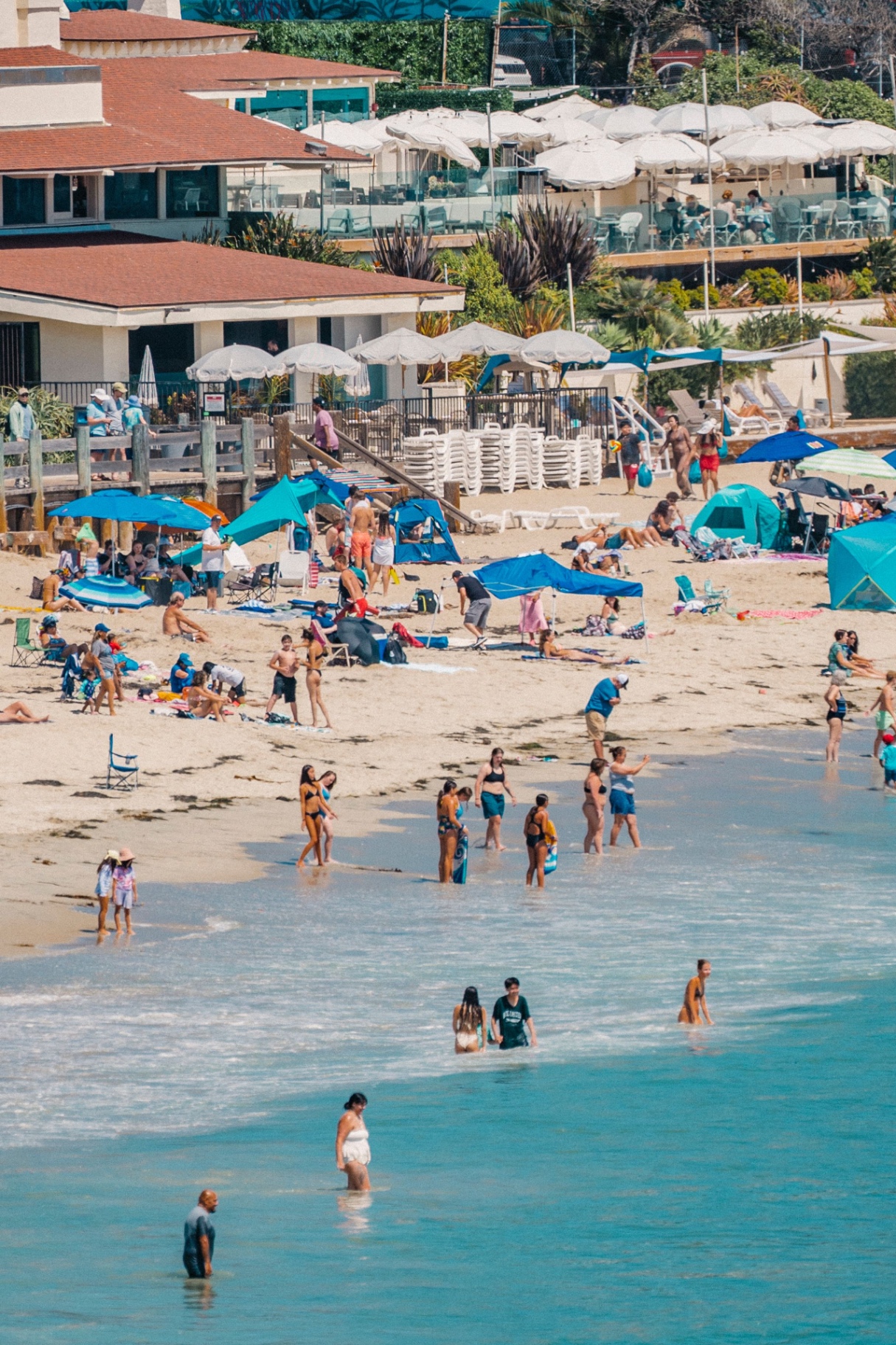 Swimmers and beach umbrellas in clear turquoise water below a coastal clubhouse