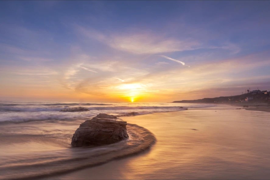 Sun dropping into the Pacific behind a sea rock on a glassy shoreline