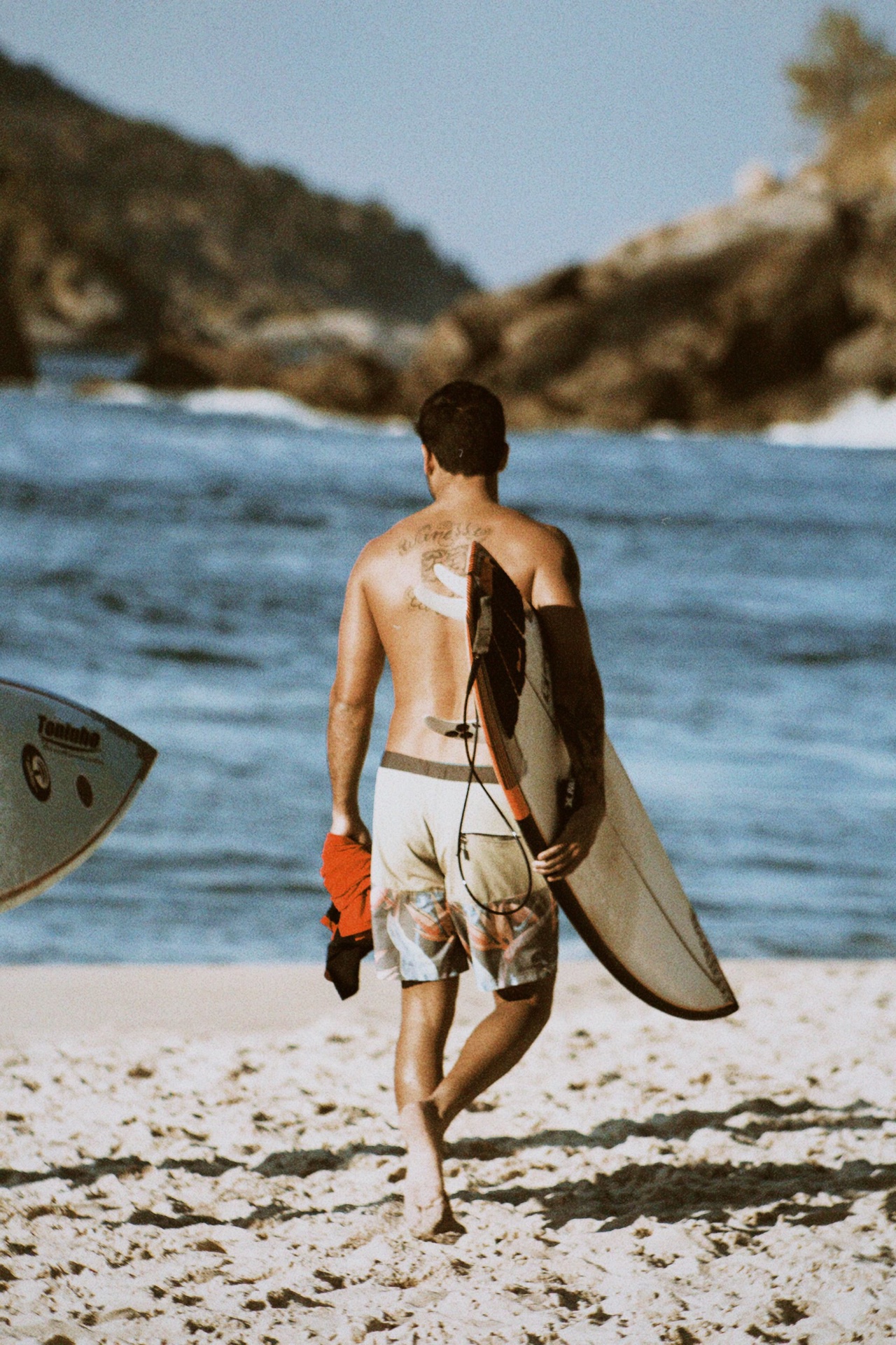 Surfer carrying a board along the sand toward a rocky point break