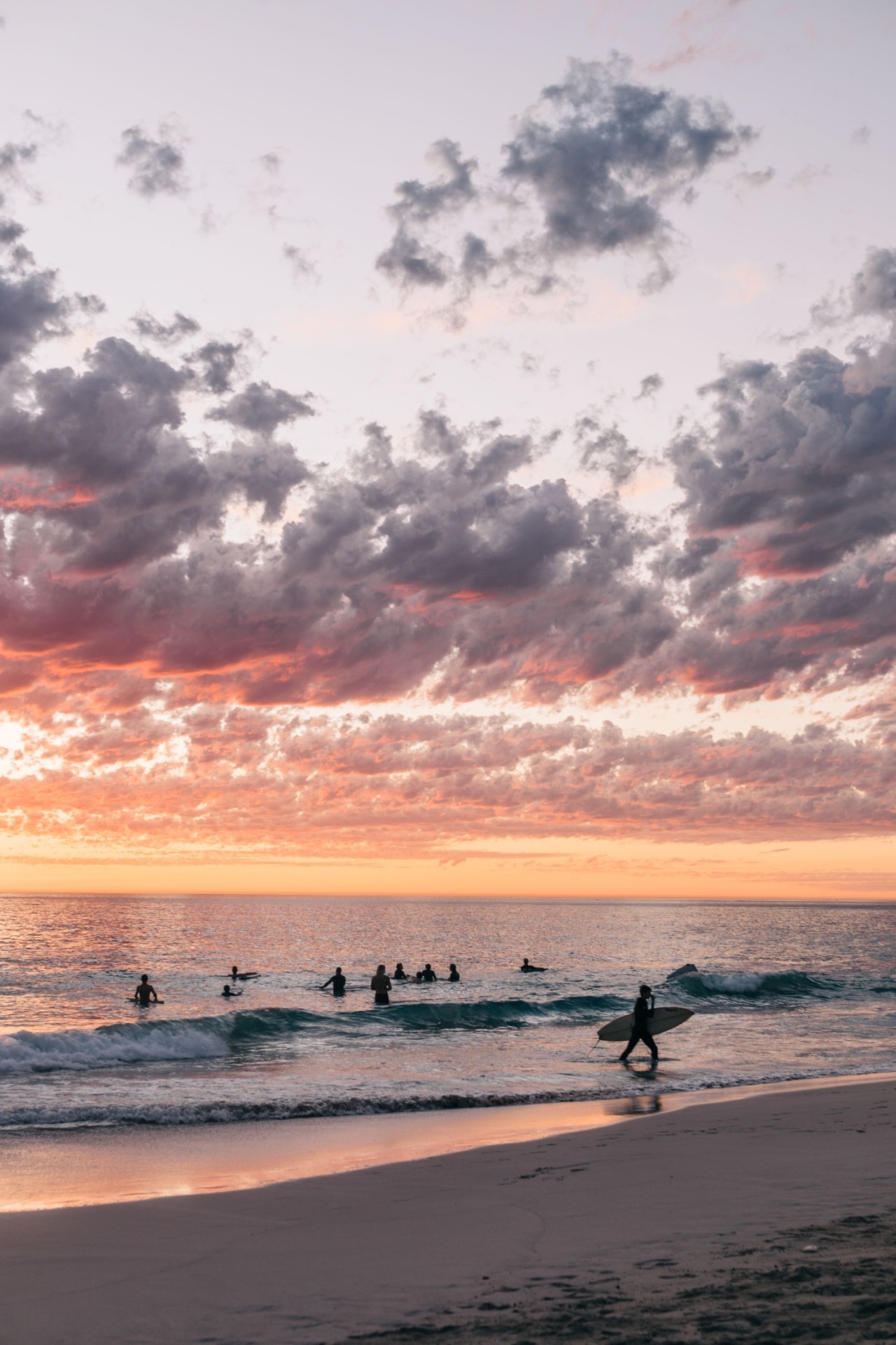 Surfers waiting in the lineup under a pink and gold sunset sky