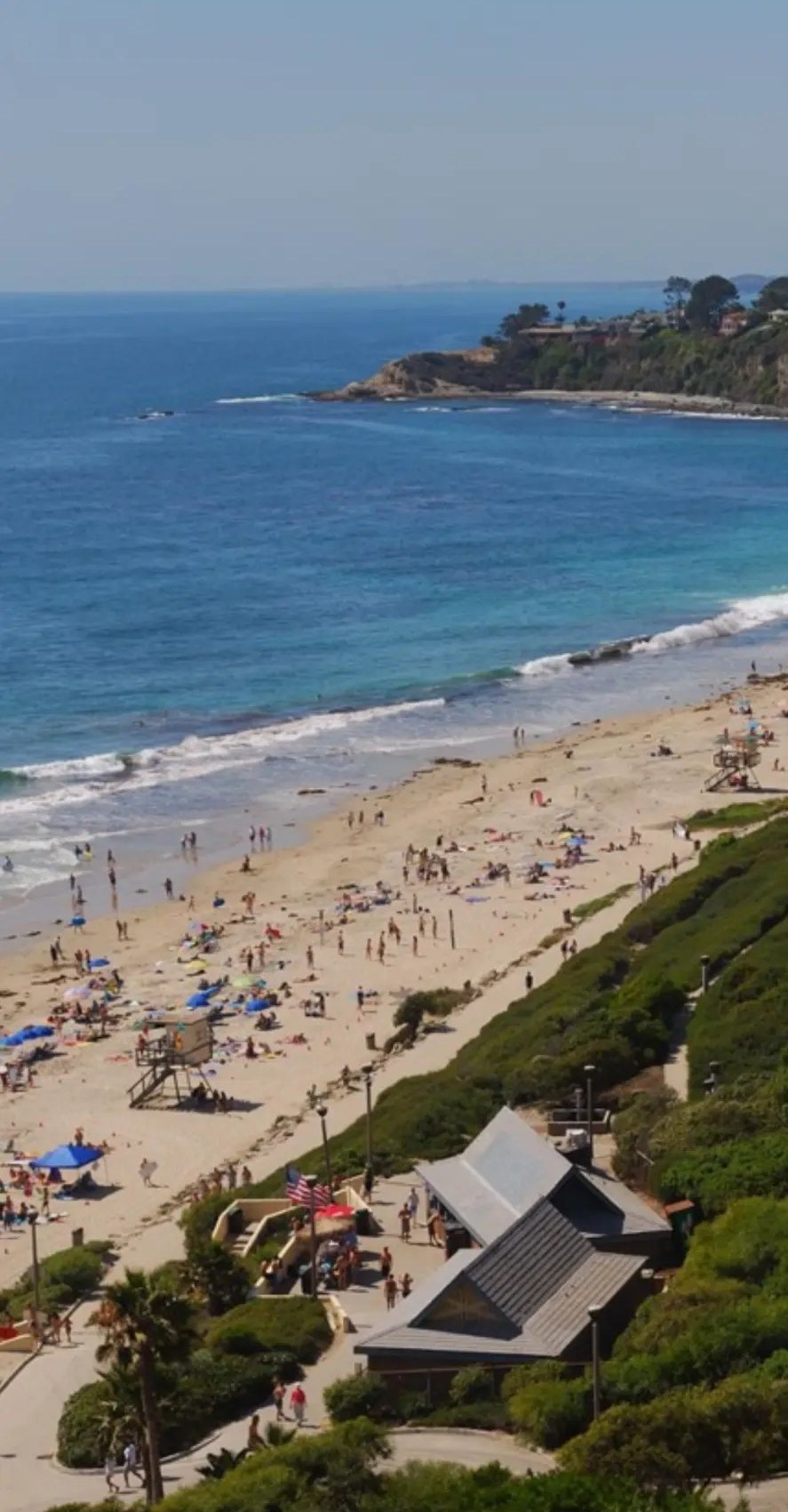 Aerial view of a wide Laguna beach cove with umbrellas and bluff trail